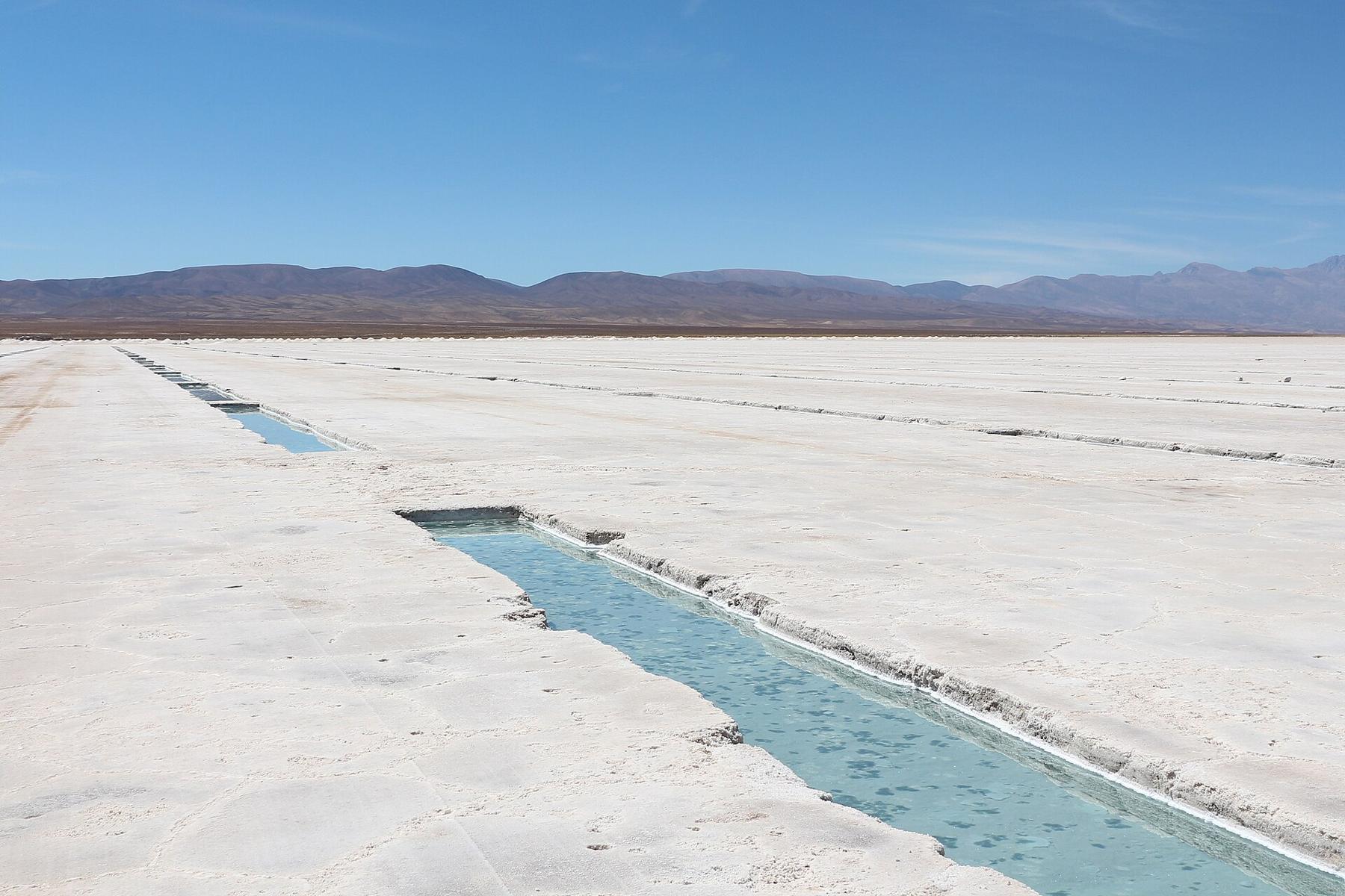 Salina blanca con piletas de agua y montañas al fondo